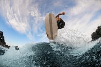 beautiful view of a wakesurf board and a male athlete jumping in the air above a splashing wave